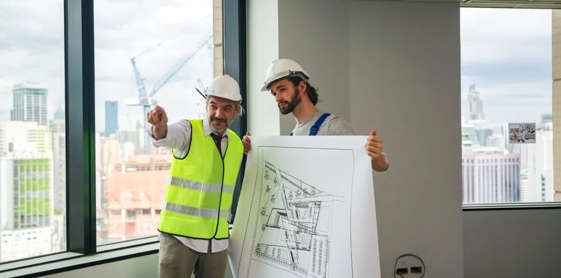 Profesionales de SIAGT revisando planos arquitectónicos con un fondo de un proyecto en desarrollo.